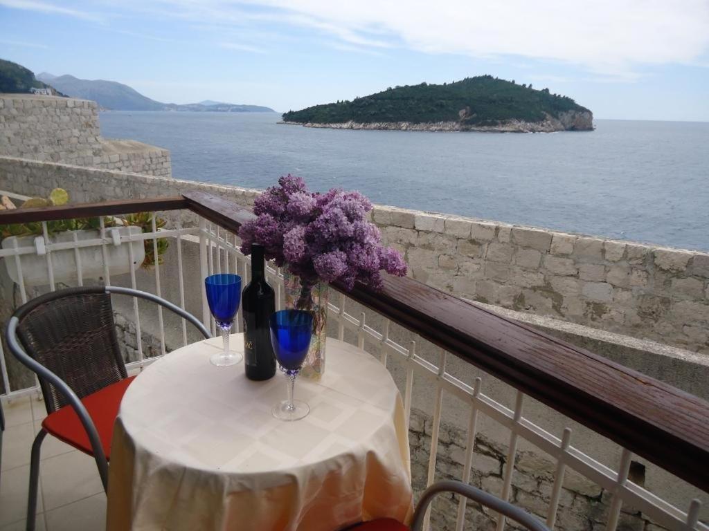 a table with two wine glasses and purple flowers on a balcony at Apartments Abjanic in Dubrovnik