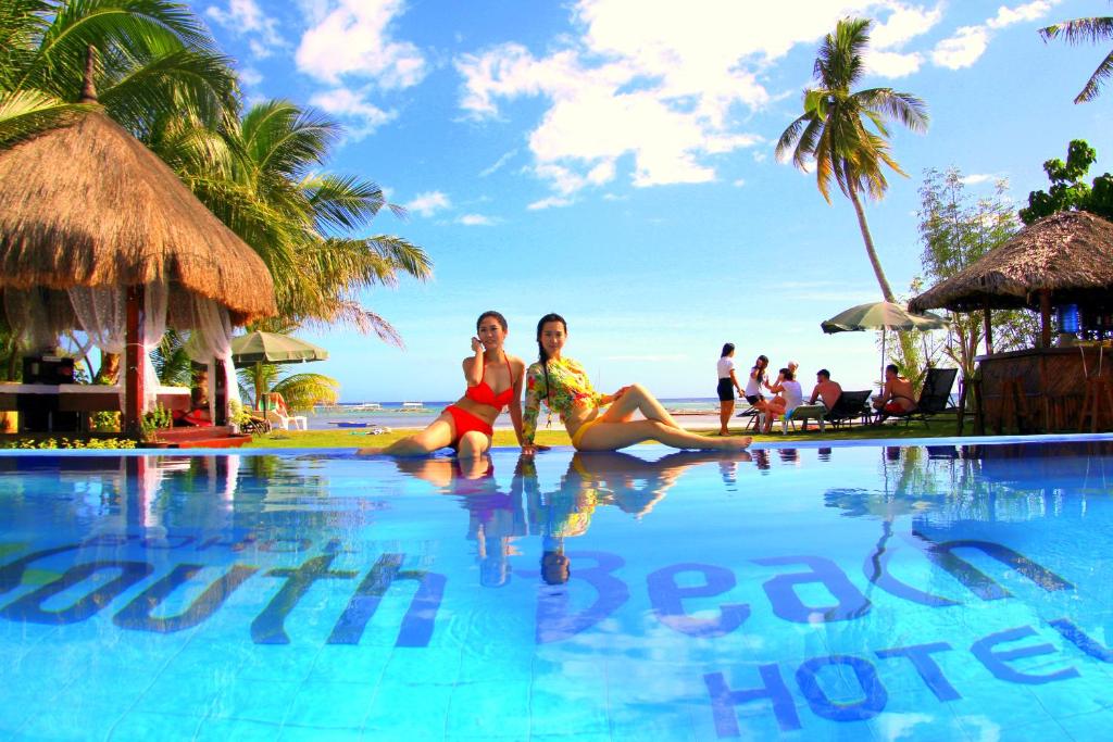 dos mujeres sentadas en el borde de una piscina en un complejo en Bohol South Beach Hotel en Panglao