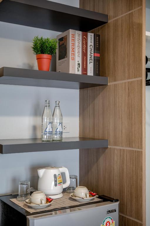 A compact in-room beverage station with a kettle, cups, bottled water and open shelves.