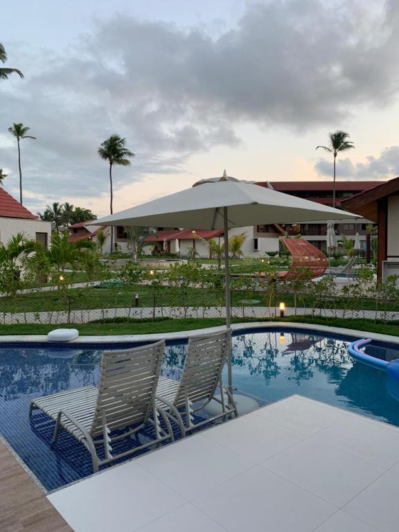 a swimming pool with two chairs and an umbrella at Oka Muro Alto in Porto De Galinhas