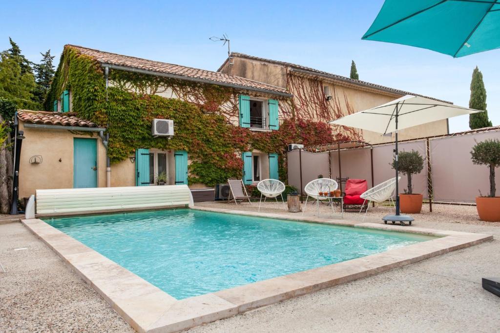 uma piscina em frente a uma casa com cadeiras e um guarda-sol em Villa de 3 chambres avec piscine privee jardin clos et wifi a Beaumes de Venise em Beaumes-de-Venise