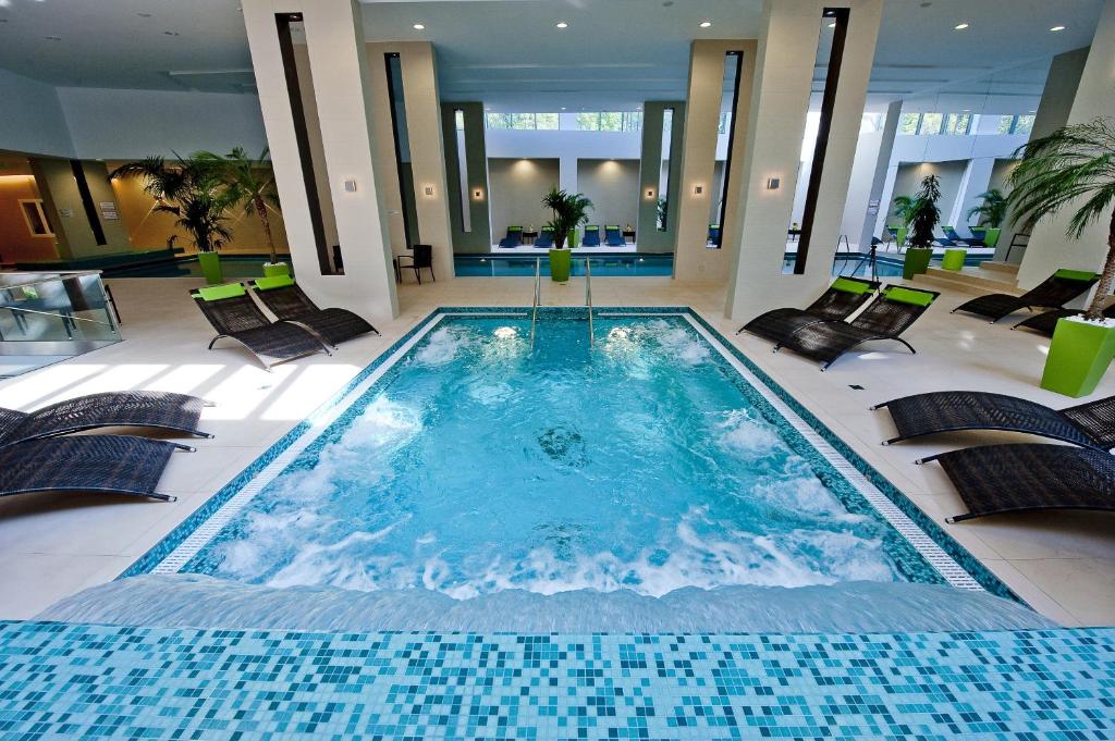 a large swimming pool in a hotel lobby with chairs at Abacus Business & Wellness Hotel in Herceghalom