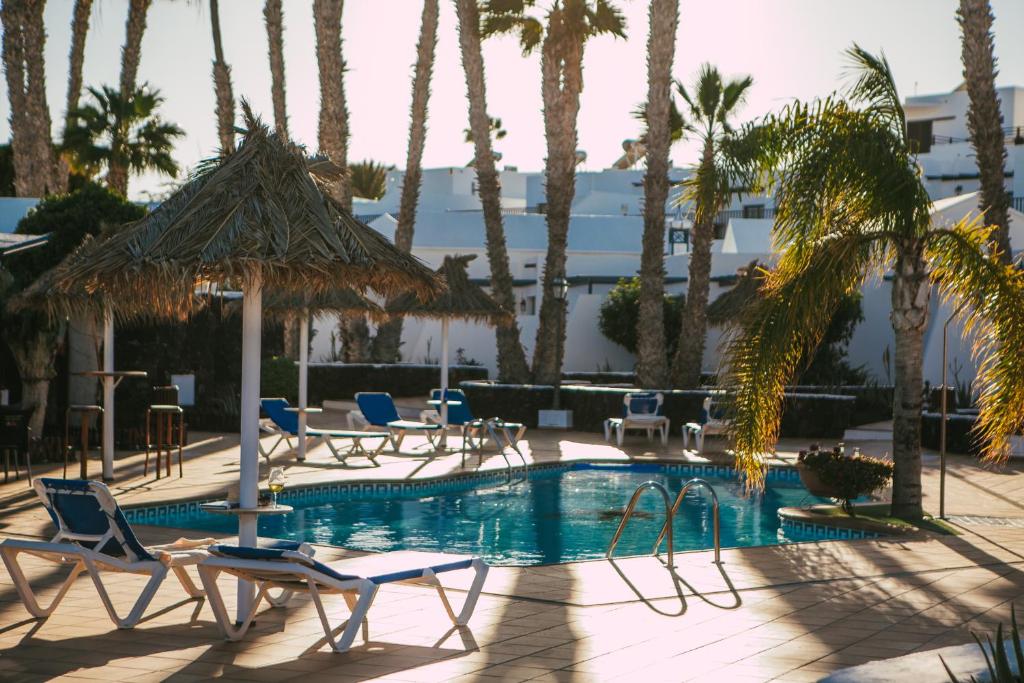 a swimming pool with chairs and palm trees at Mar Azul Playa in Puerto del Carmen