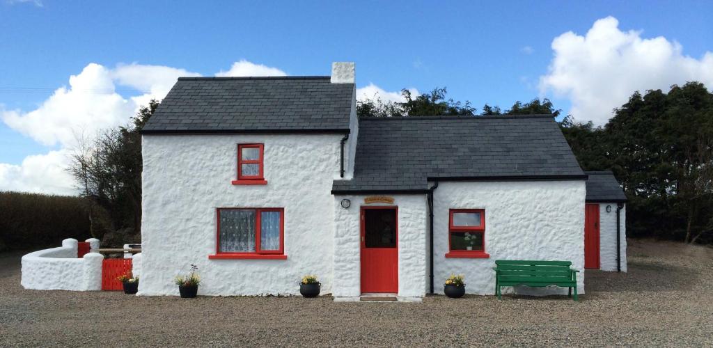 una pequeña casa blanca con una puerta roja y un banco verde en Cobblers Cottage Creggan, en Greencastle