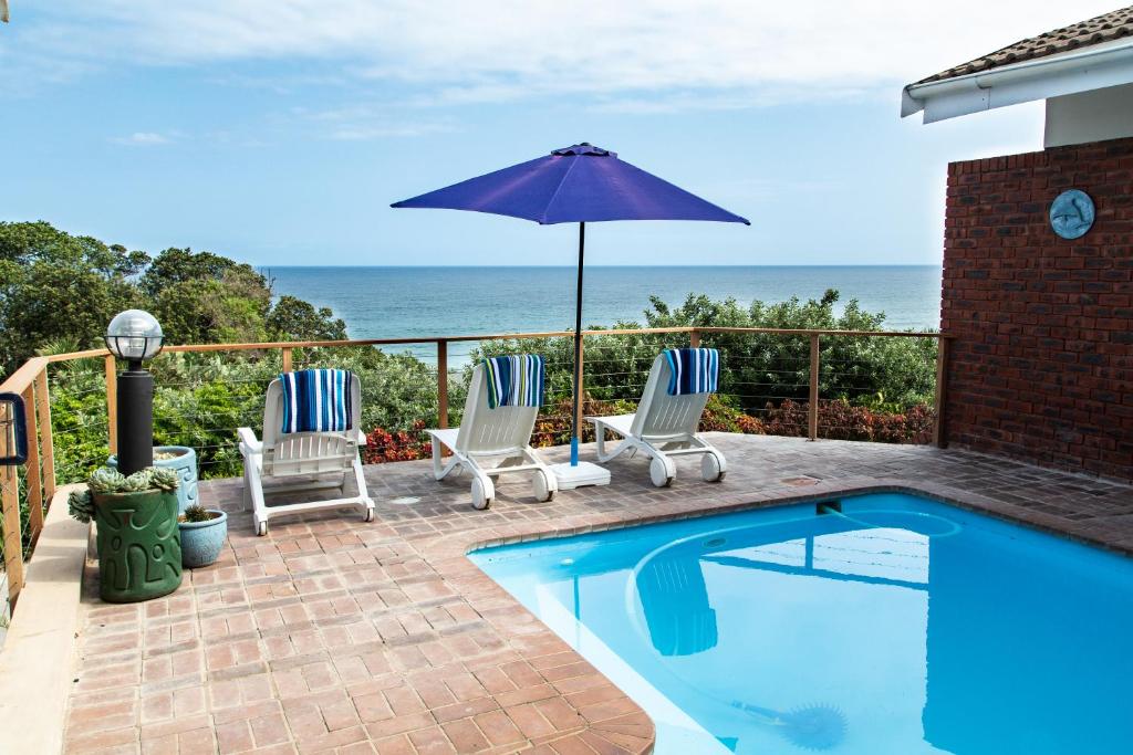 a swimming pool with two chairs and an umbrella at Sea View townhouse in Zinkwazi Beach in Zinkwazi Beach