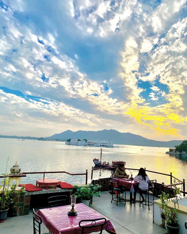 two people sitting at tables on a deck near the water at Lalghat Haveli in Udaipur