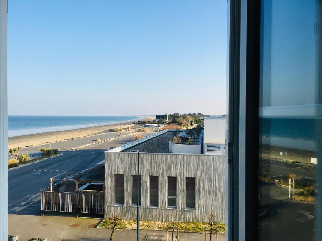 a view of a building and the beach from a window at Studio Les Pieds dans l'eau in Donville-les-Bains