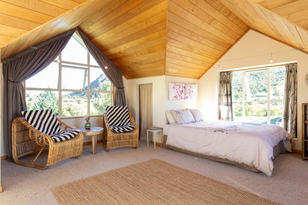 a bedroom with a bed and two chairs and windows at Riverside Retreat in Queenstown