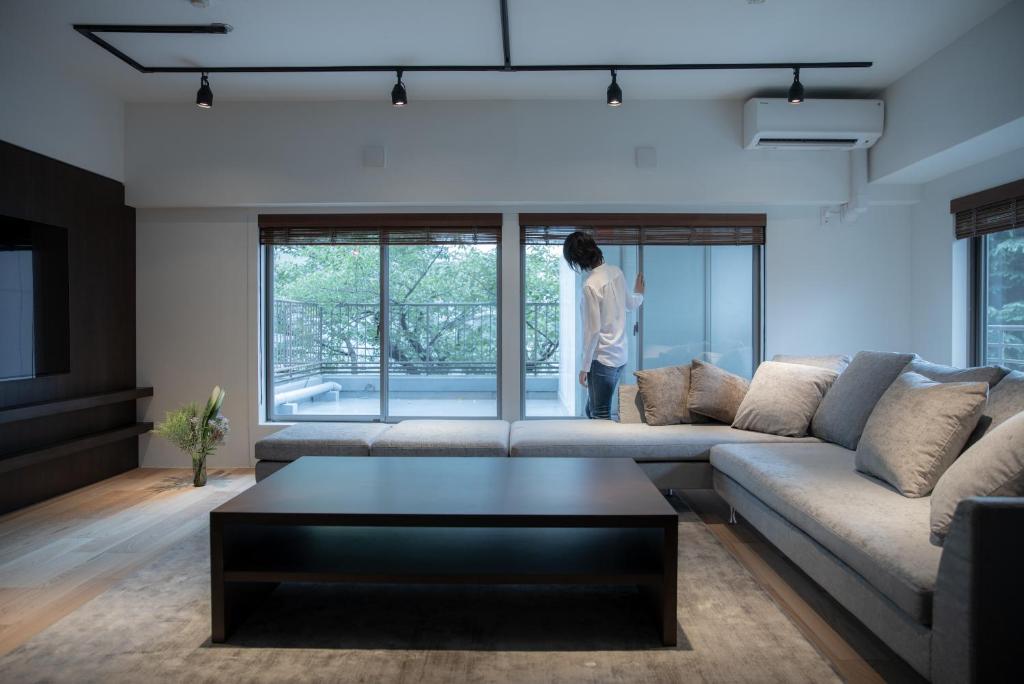 NIYS apartments 07 type في طوكيو: شخص واقف في غرفة المعيشة ينظر من النافذة