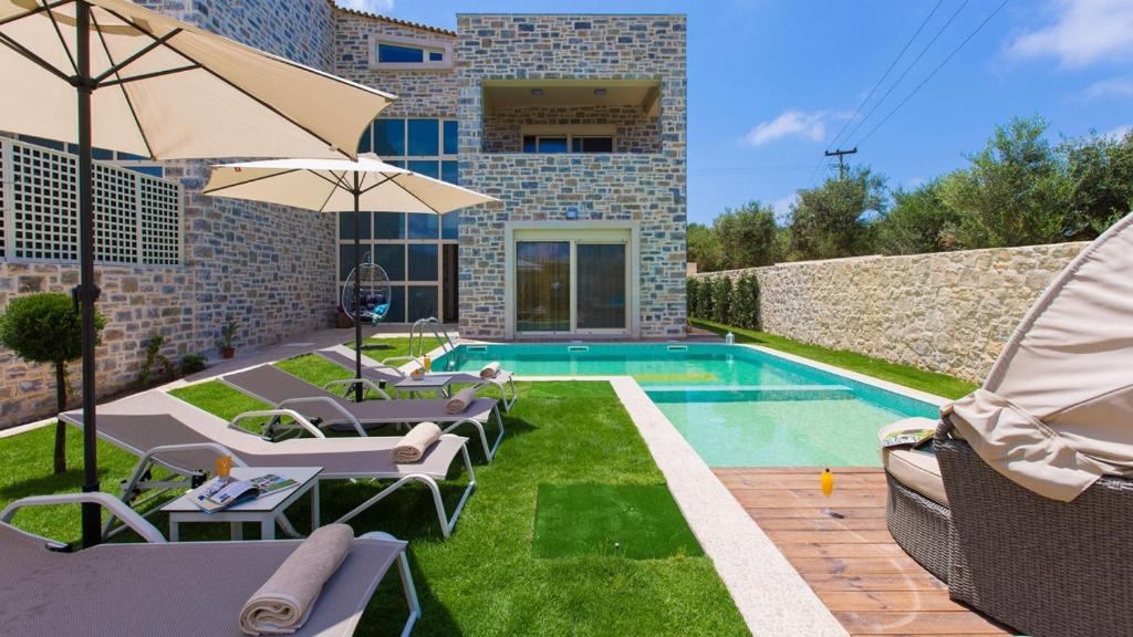 a pool with chairs and an umbrella next to a building at Blue Mare Villa Rethimno in Magnisía