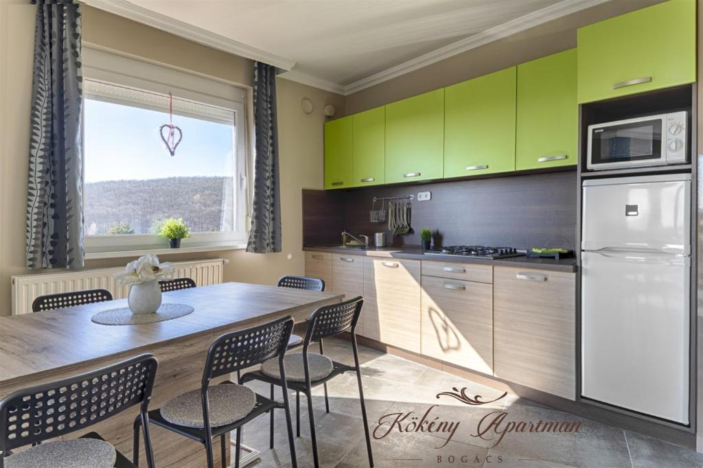 ボガーチにあるKökény Apartman Bogácsのキッチン(緑のキャビネット、テーブル、椅子付)