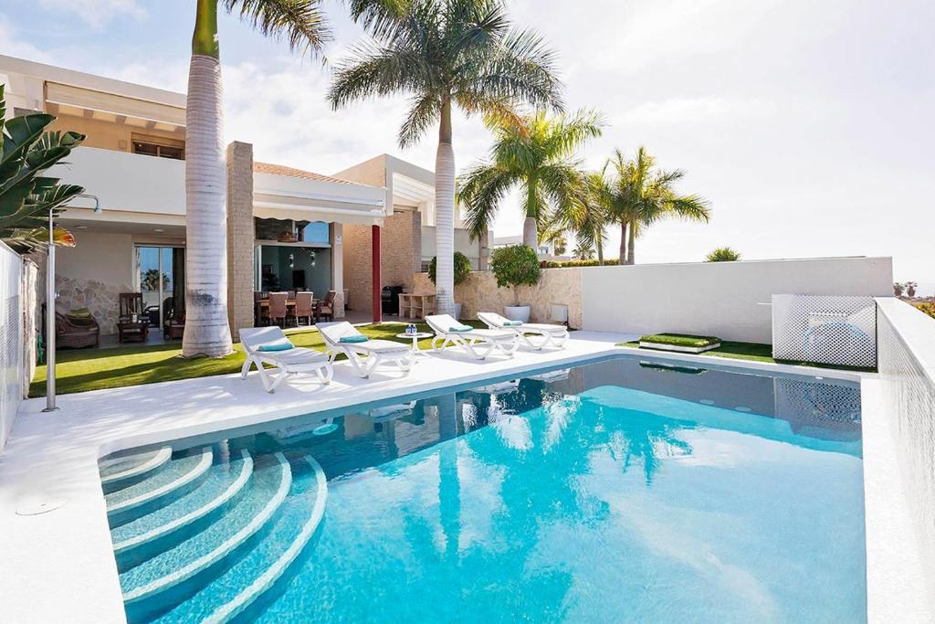 a swimming pool with chairs and a house at Villa La Caleta Golf in Adeje
