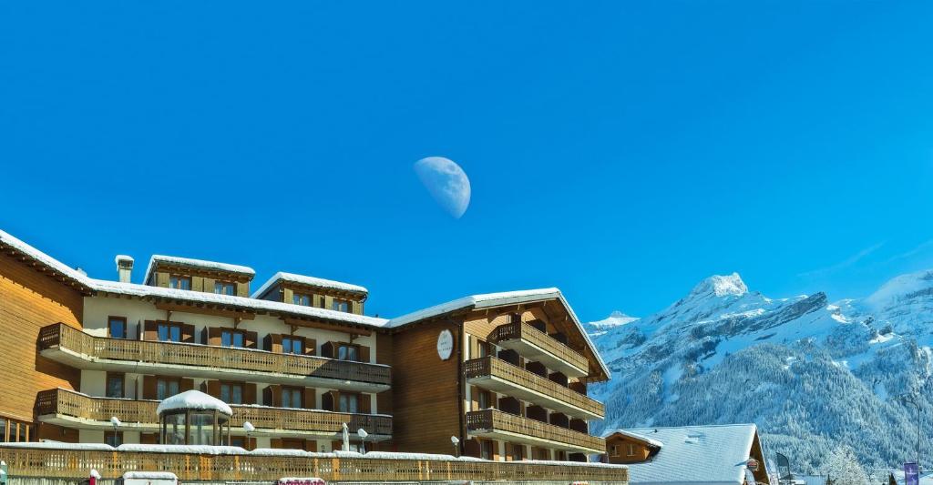 un grand bâtiment avec une montagne en arrière-plan dans l'établissement Le Chamois, aux Diablerets