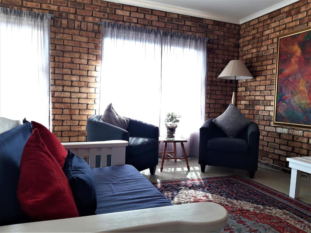 a living room with a couch and chairs and a brick wall at Beaufort 8 in Jeffreys Bay