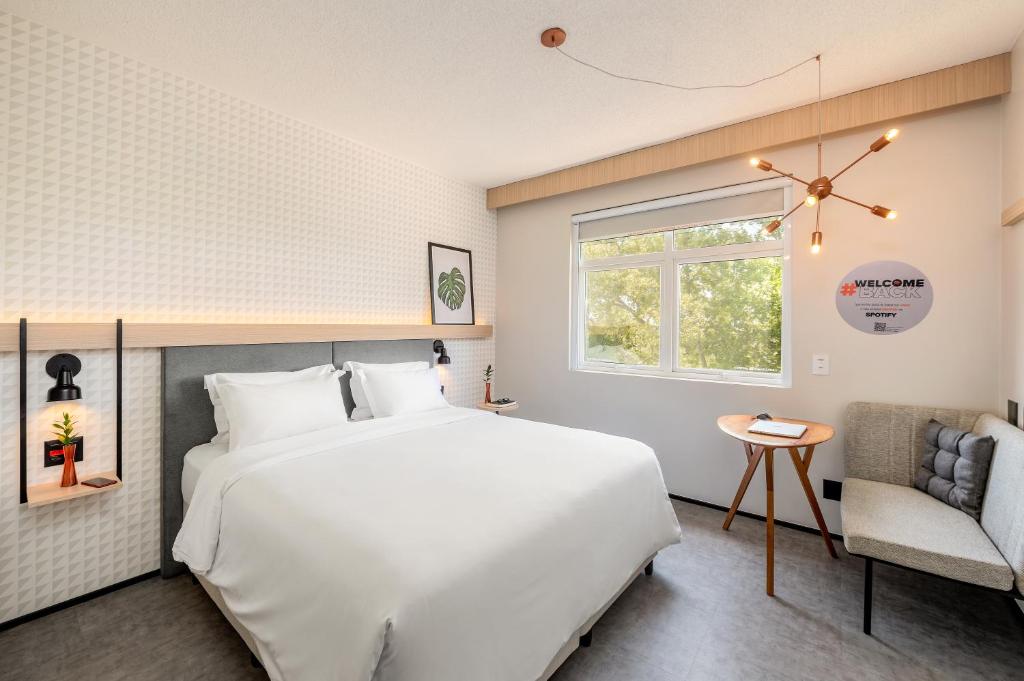 a bedroom with a large white bed and a chair at Intercity Porto Alegre Aeroporto in Porto Alegre