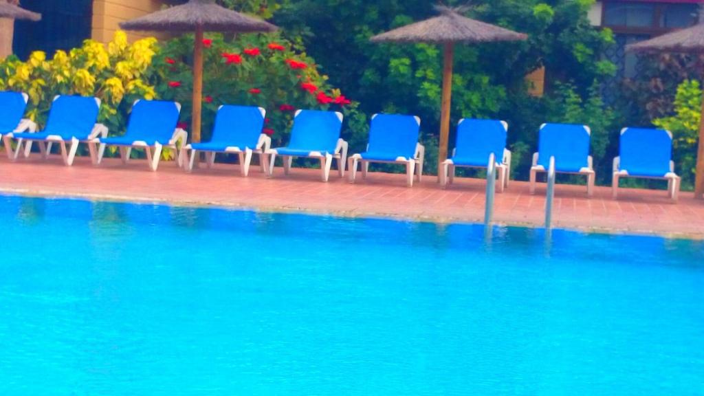 eine Gruppe blauer Stühle und Sonnenschirme neben einem Pool in der Unterkunft Apartamento Hércules in Costa Del Silencio