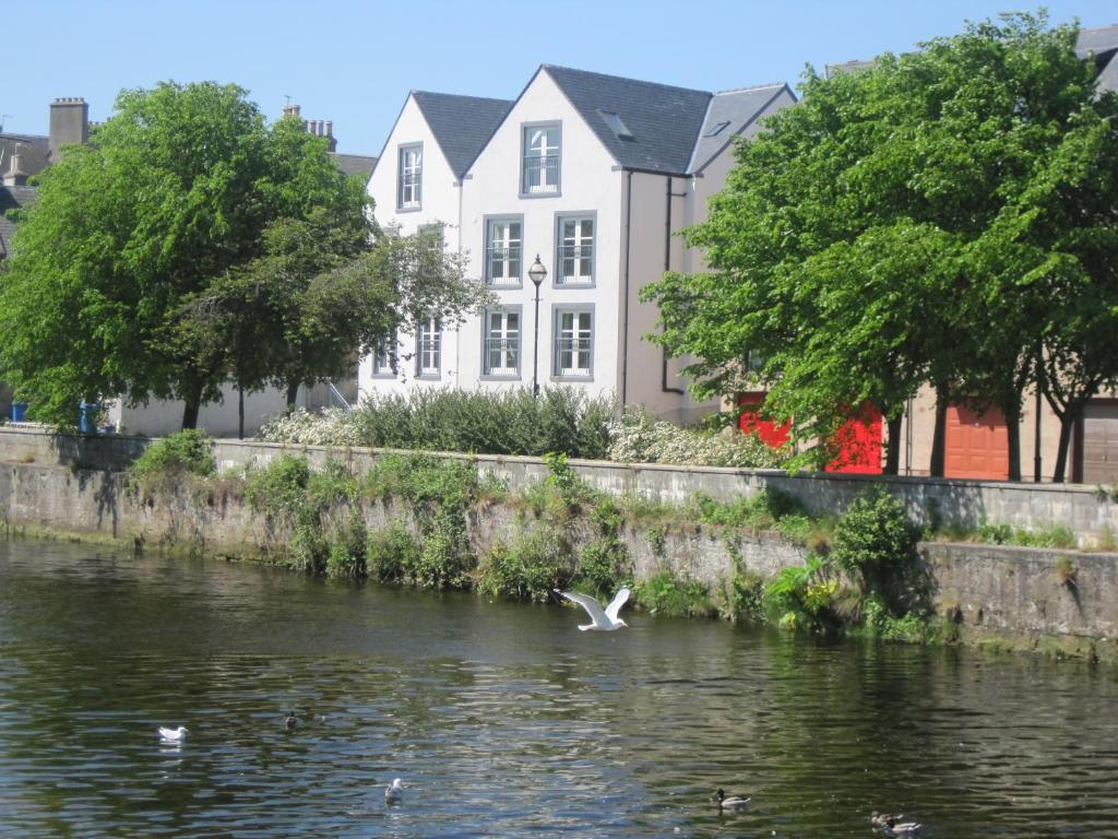 a bird flying over a river in front of a building at Luxury Riverbank Apartment, Nairn in Nairn