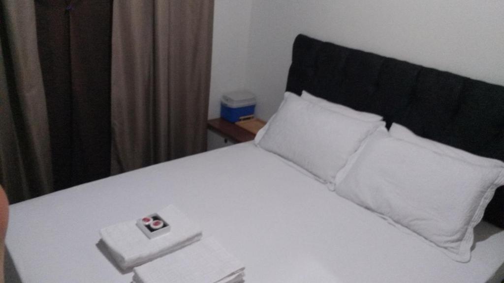 a white bed with a black headboard and white pillows at Hospedom Mazzoca 02 , WC compartilhado in Itapema
