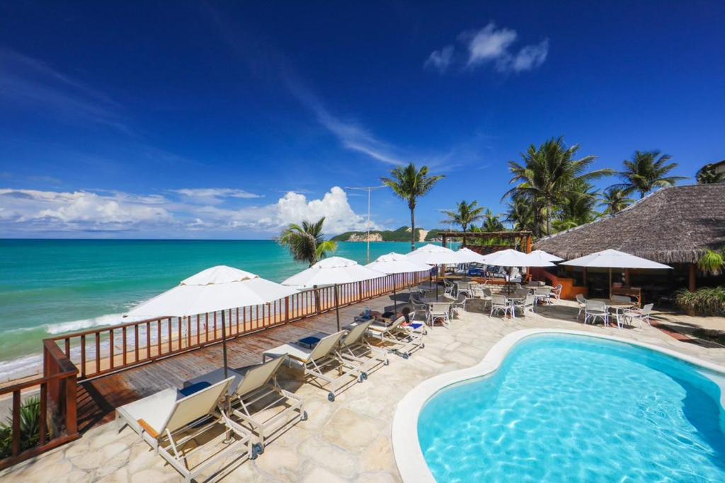 a swimming pool with chairs and umbrellas and the ocean at Manary Praia Hotel in Natal