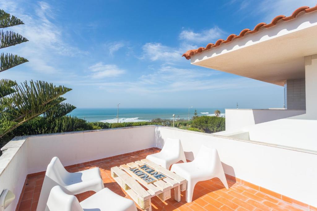 Un balcón con sillas blancas y una mesa. en Blue Buddha Beach House, en Ericeira