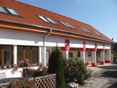 a white building with a red roof and some plants at Penzion Loučka in Rajhradice