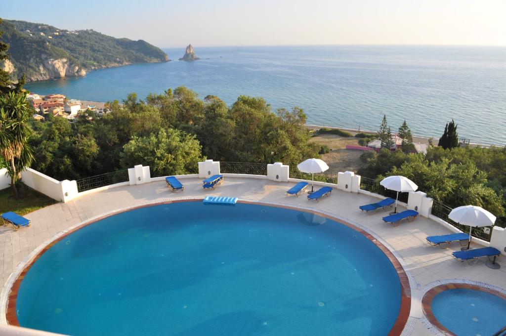 a swimming pool with chairs and umbrellas and the ocean at Holiday Apartments Maria with pool and Panorama View - Agios Gordios Beach in Agios Gordios