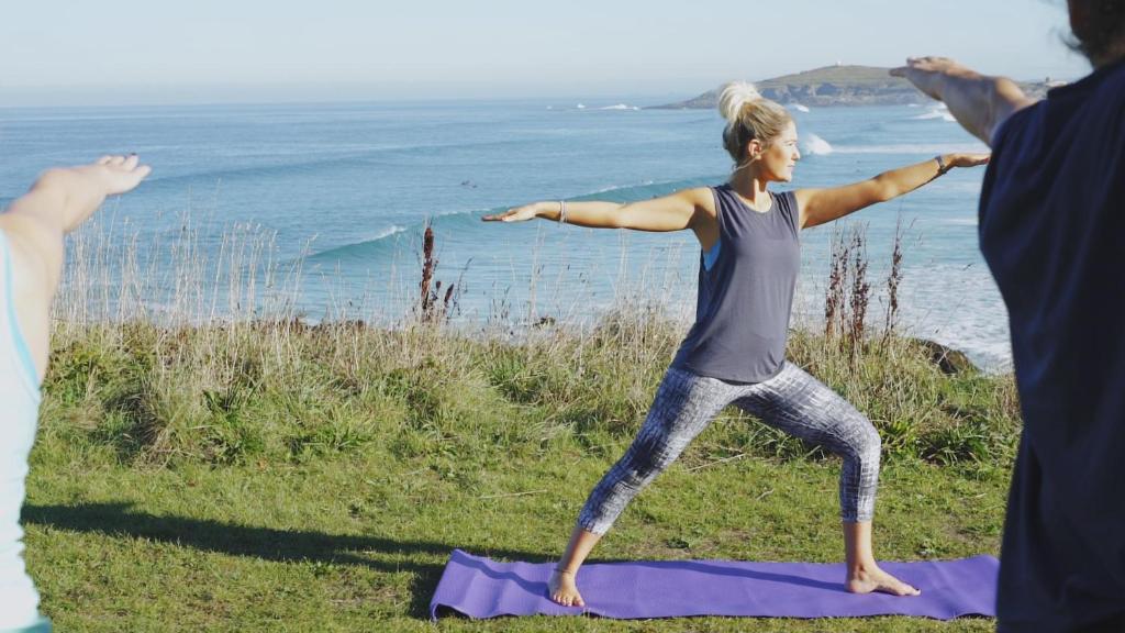 a woman doing yoga on a purple yoga mat near the ocean at Fistral Beach Hotel and Spa - Adults Only in Newquay