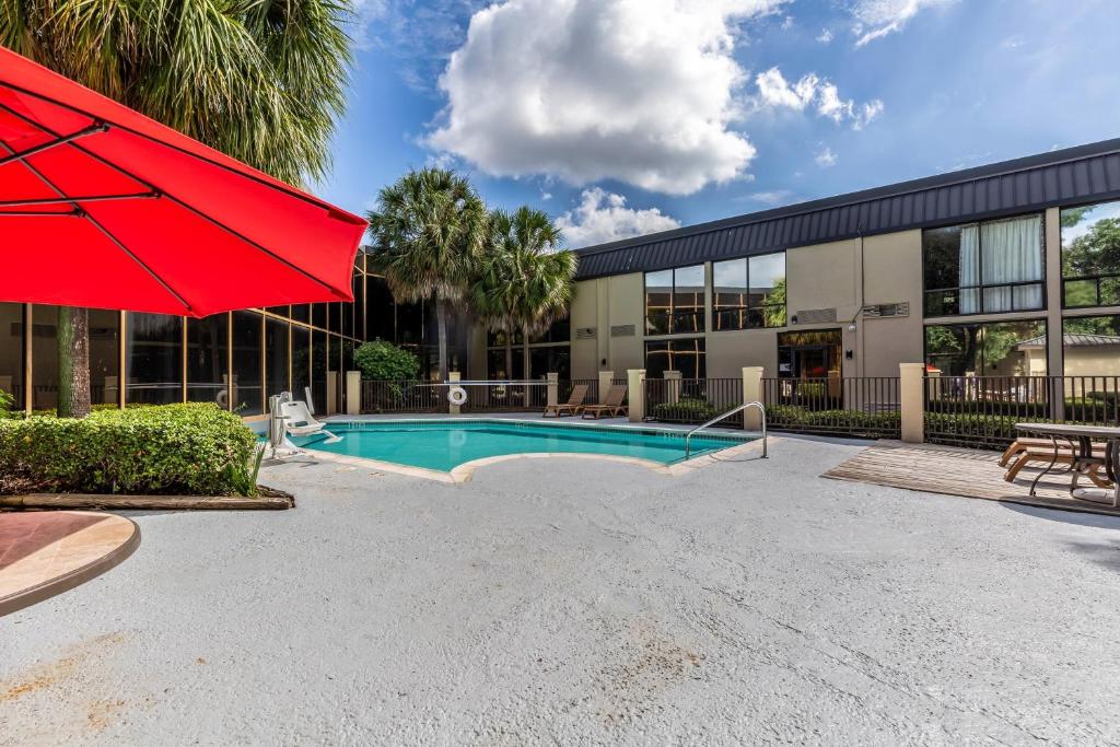 a pool in front of a building with a red umbrella at Red Roof Inn PLUS & Suites Houston - IAH Airport SW in Houston