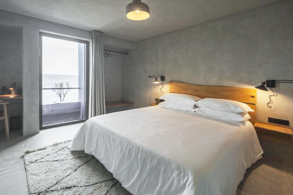 a bedroom with a large white bed with a large window at CASA DA ILHA - Slow Living Residence & Suites in Ponta Delgada