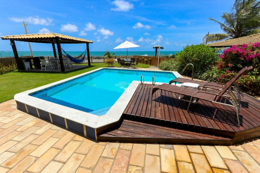 a swimming pool with a deck and chairs and the ocean at Casa a beira mar com 4 suites e muito conforto in Porto De Galinhas