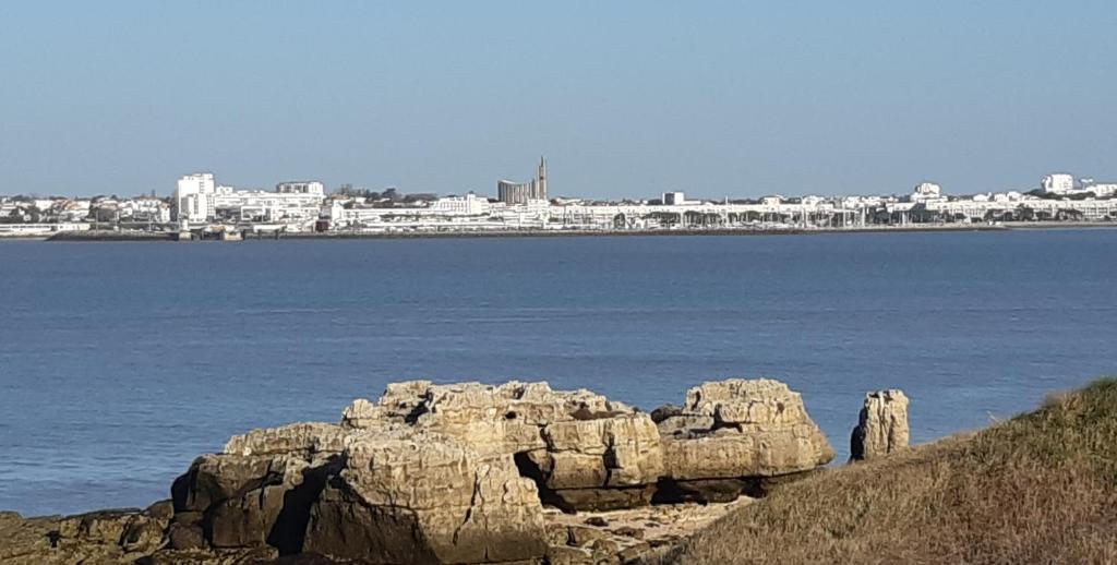 un groupe de rochers dans l'eau avec une ville en arrière-plan dans l'établissement Le val joyeux, à Royan