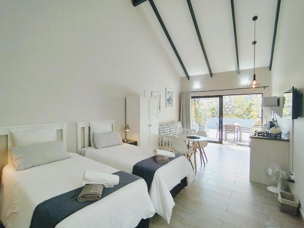 a bedroom with two beds and a table and a balcony at Capricorn Studio Two - 150m to Solar Beach, Patio & Braai, Wifi, DSTV & Netflix in Plettenberg Bay