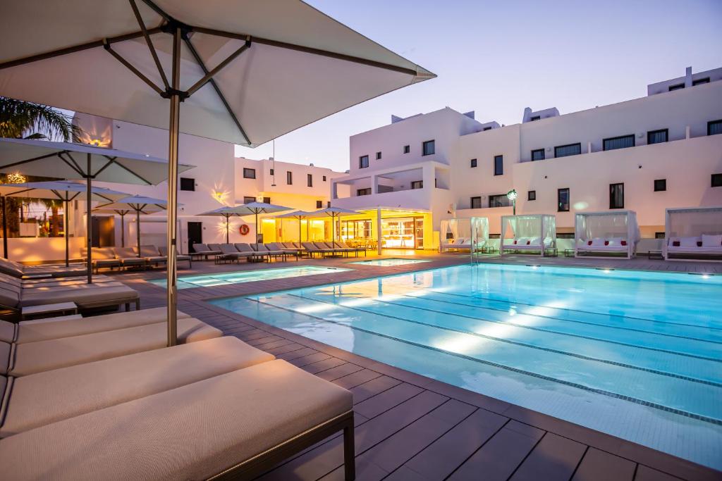 ein großer Pool mit Stühlen und einem Sonnenschirm in der Unterkunft Migjorn Ibiza Suites & Spa in Playa d'en Bossa