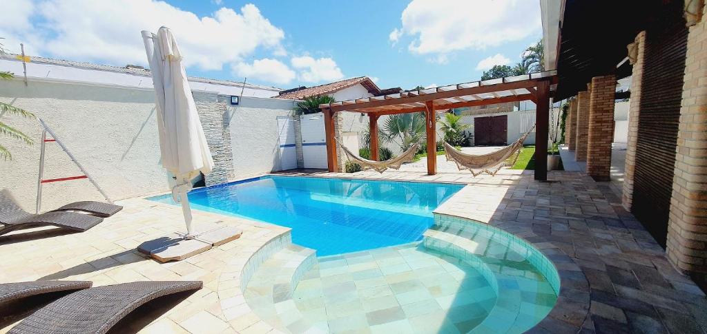 a swimming pool with two chairs and an umbrella at Espetacular, 6 suítes, Varanda Gourmet, Bilhar, Pebolim, Praia dos Sonhos in Itanhaém