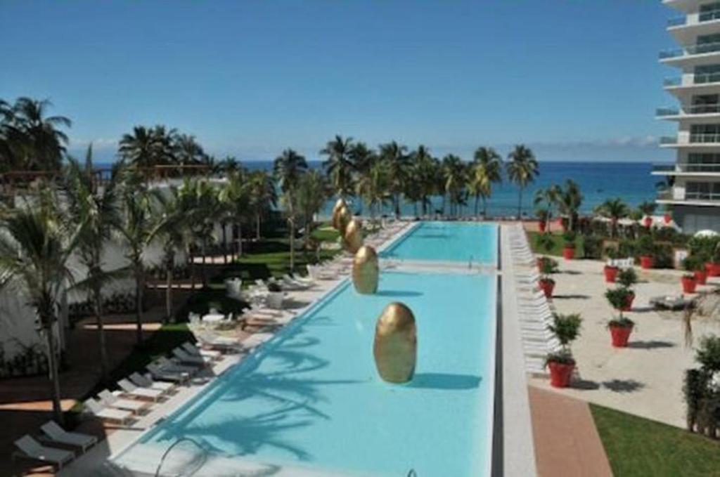 a swimming pool at a resort with palm trees and the ocean at Departamentos Oceanfront Icon Vallarta in Puerto Vallarta