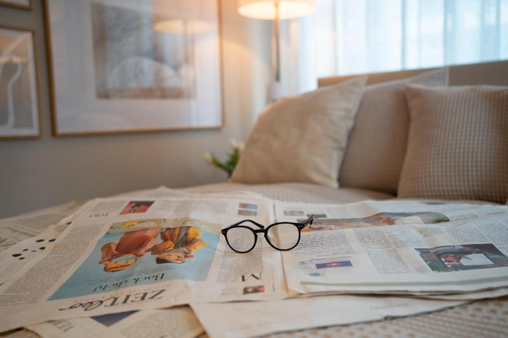 parę okularów siedzących na łóżku na górze gazety w obiekcie Studio-Apartment Piccolino 26 w mieście Timmendorfer Strand