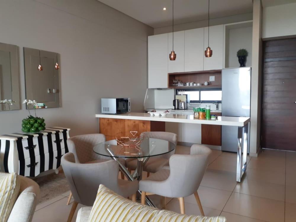 uma cozinha com uma mesa de vidro e algumas cadeiras em Zimbali Suite 606 em Ballito