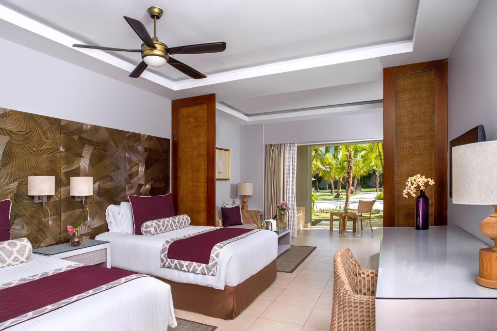 Spacious hotel suite with twin beds, wooden accents, and ocean view balcony access.