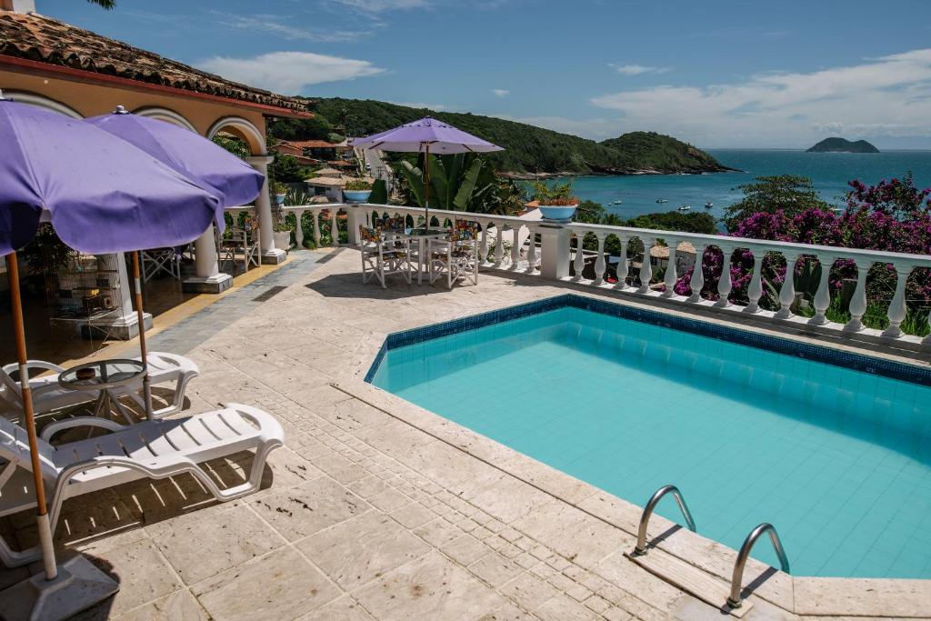 a swimming pool with chairs and umbrellas and the ocean at Casagrande Hotel Boutique in Búzios