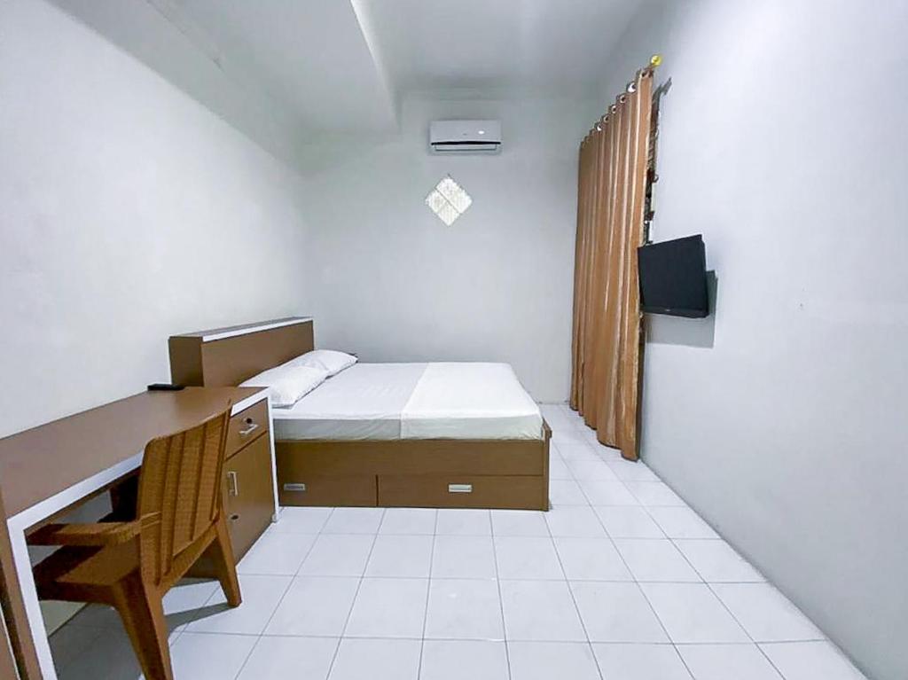 Habitación pequeña con cama, escritorio y TV. en Damigalova Guest House Mitra RedDoorz, en Jambi