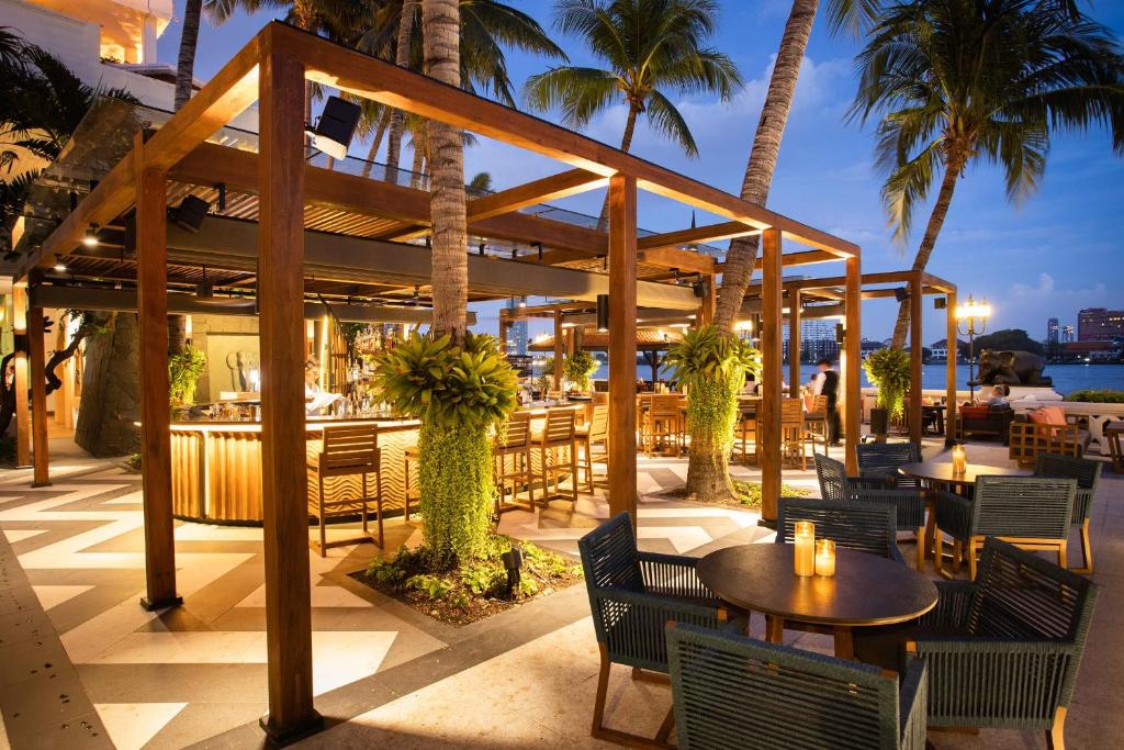 a restaurant with tables and chairs and palm trees at Anantara Riverside Bangkok Resort in Bangkok