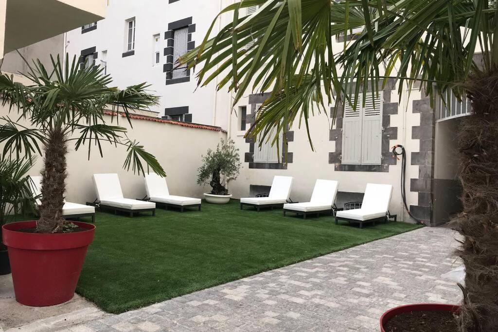 un patio con sillas blancas y una palmera en NID D AMOUR F1 40m2 calme RDC possibilité jacuzzi hammam, en Chamalières
