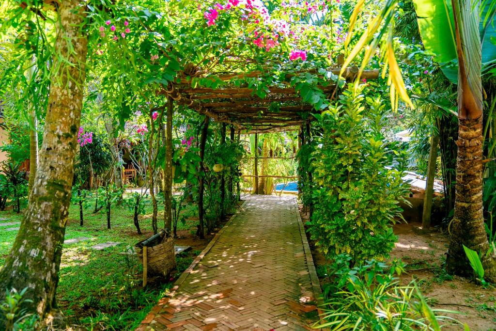 a garden with a wooden arch with pink flowers at La Mer Resort, Phú Quốc in Phú Quốc