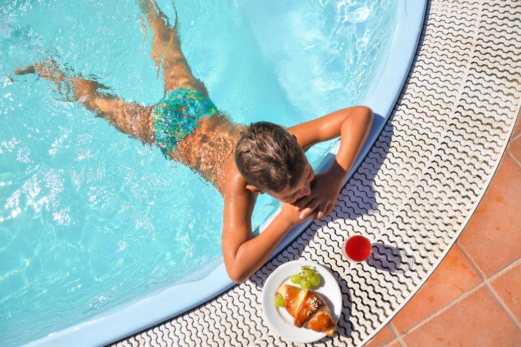 een jongen in een zwembad met een bord eten bij Villa Erade in Ischia