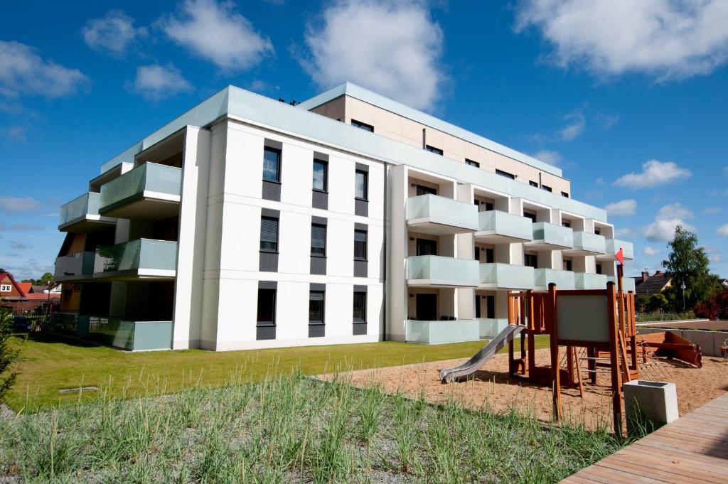 ein weißes Gebäude mit einem Spielplatz davor in der Unterkunft Apartament IKAR z widokiem na morze w kompleksie Platinium Rewal in Rewal
