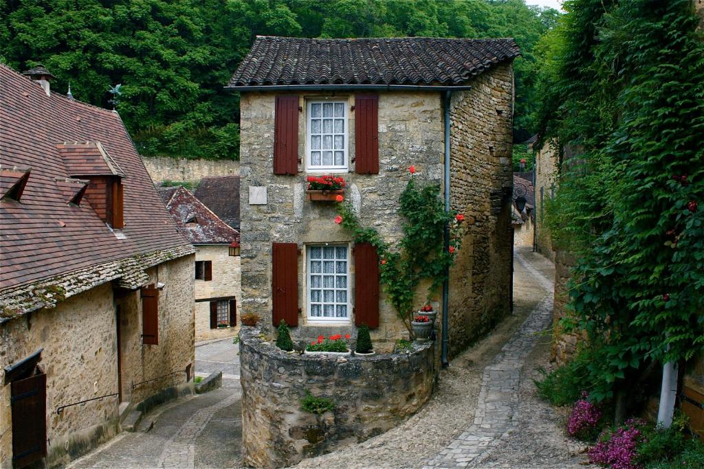 una vieja casa de piedra con persianas rojas en una calle en La Petite Maison, en Beynac-et-Cazenac
