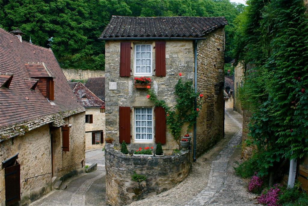 an old stone house with red shutters on a street at La Petite Maison in Beynac-et-Cazenac