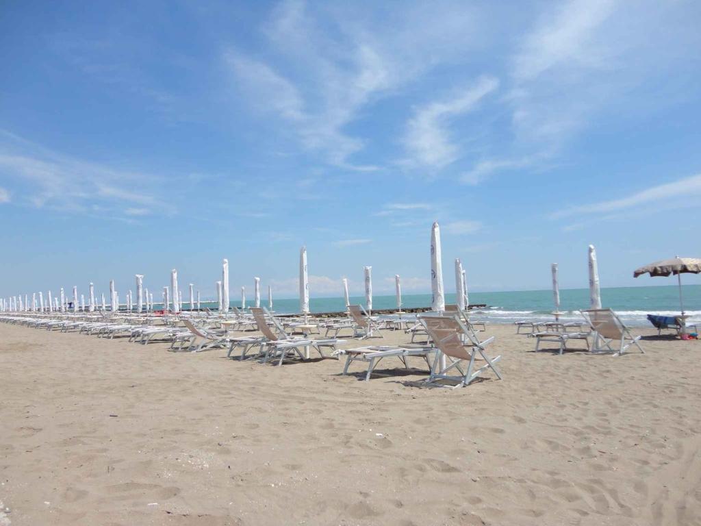 una fila di sedie e ombrelloni in spiaggia di Apartment in Porto Santa Margherita 25835 a Porto Santa Margherita di Caorle