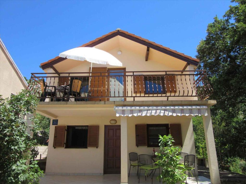 a house with a balcony with chairs and an umbrella at Apartments Karlobag/Velebit Riviera 17136 in Vidovac