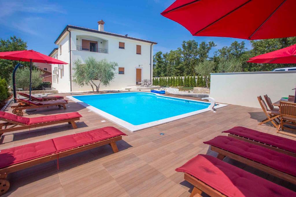 a pool with red umbrellas and chairs and a house at Apartment in Nova Vas - Istrien 35437 in Nova Vas